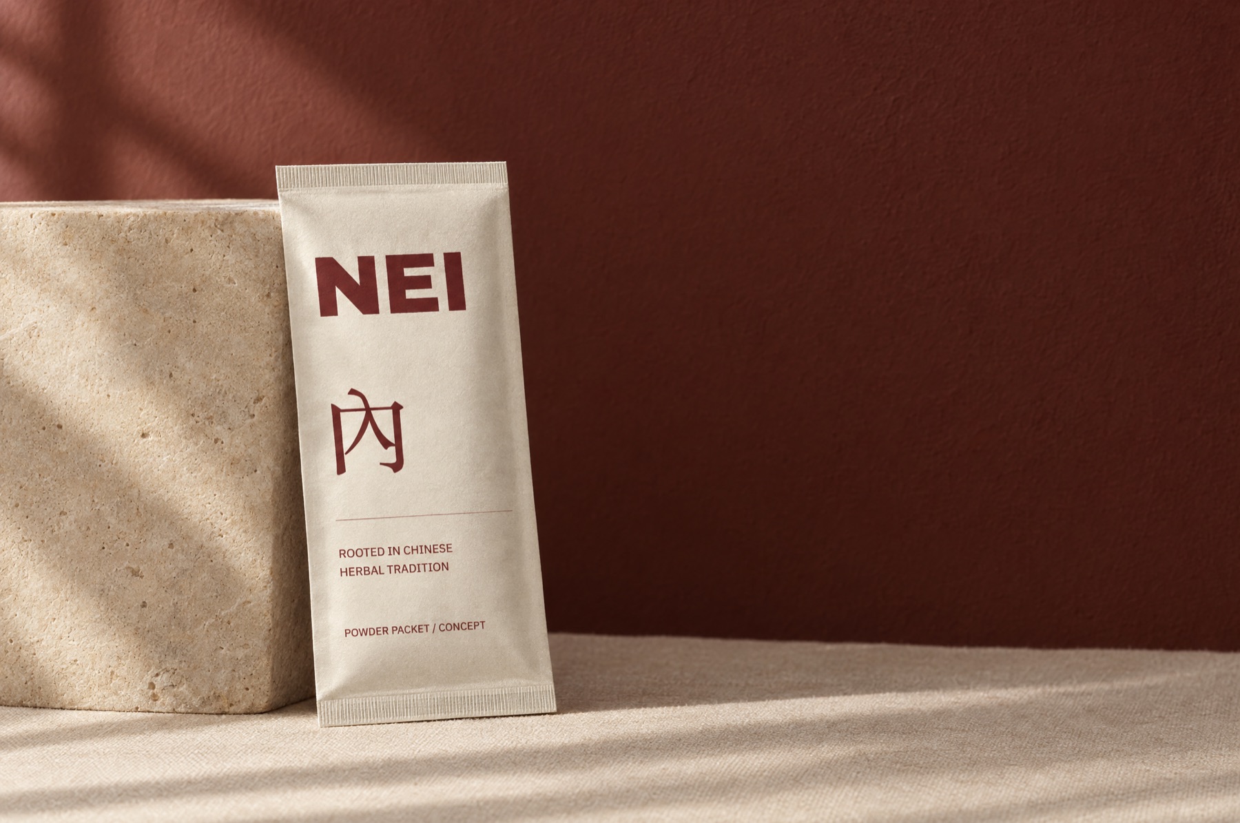 Concept photograph: a cream NEI powder packet with oxblood lettering leans on a limestone block in warm window light
